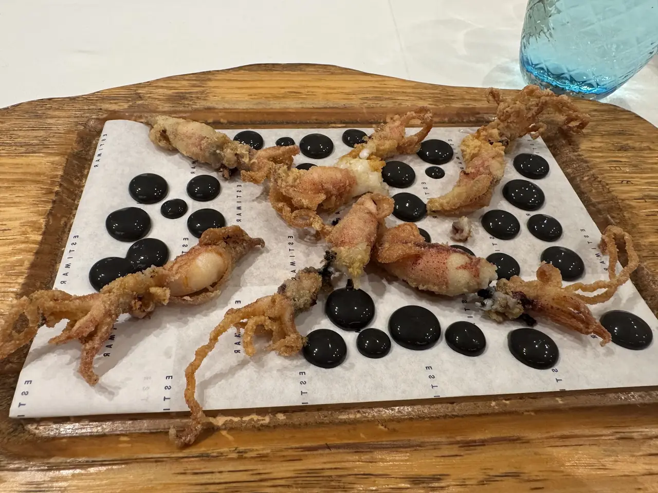 Fried baby squid served on paper with dots of dark sauce on a wooden board