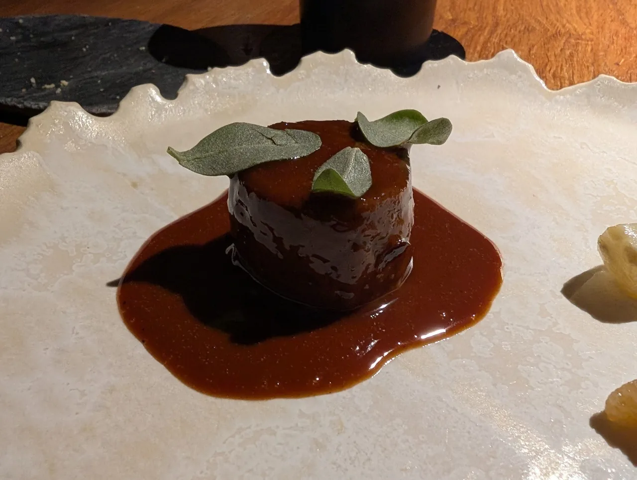 A round dark portion in glossy brown sauce with green leaves on a cream plate