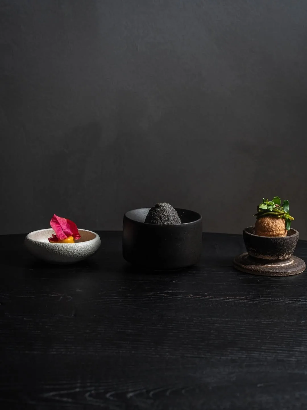 Three small dishes and a stone bowl on a black surface against a grey wall