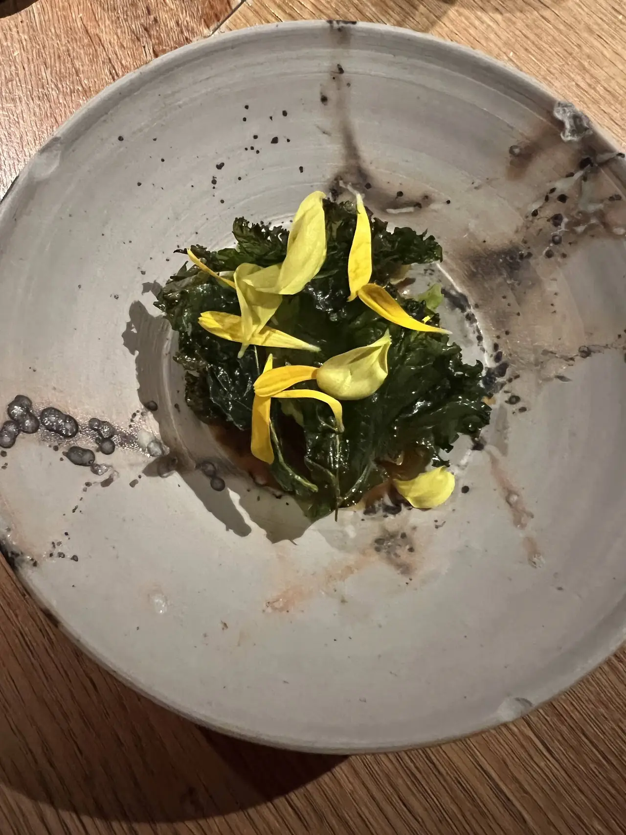 Charred kale leaves topped with yellow flower petals in a ceramic bowl
