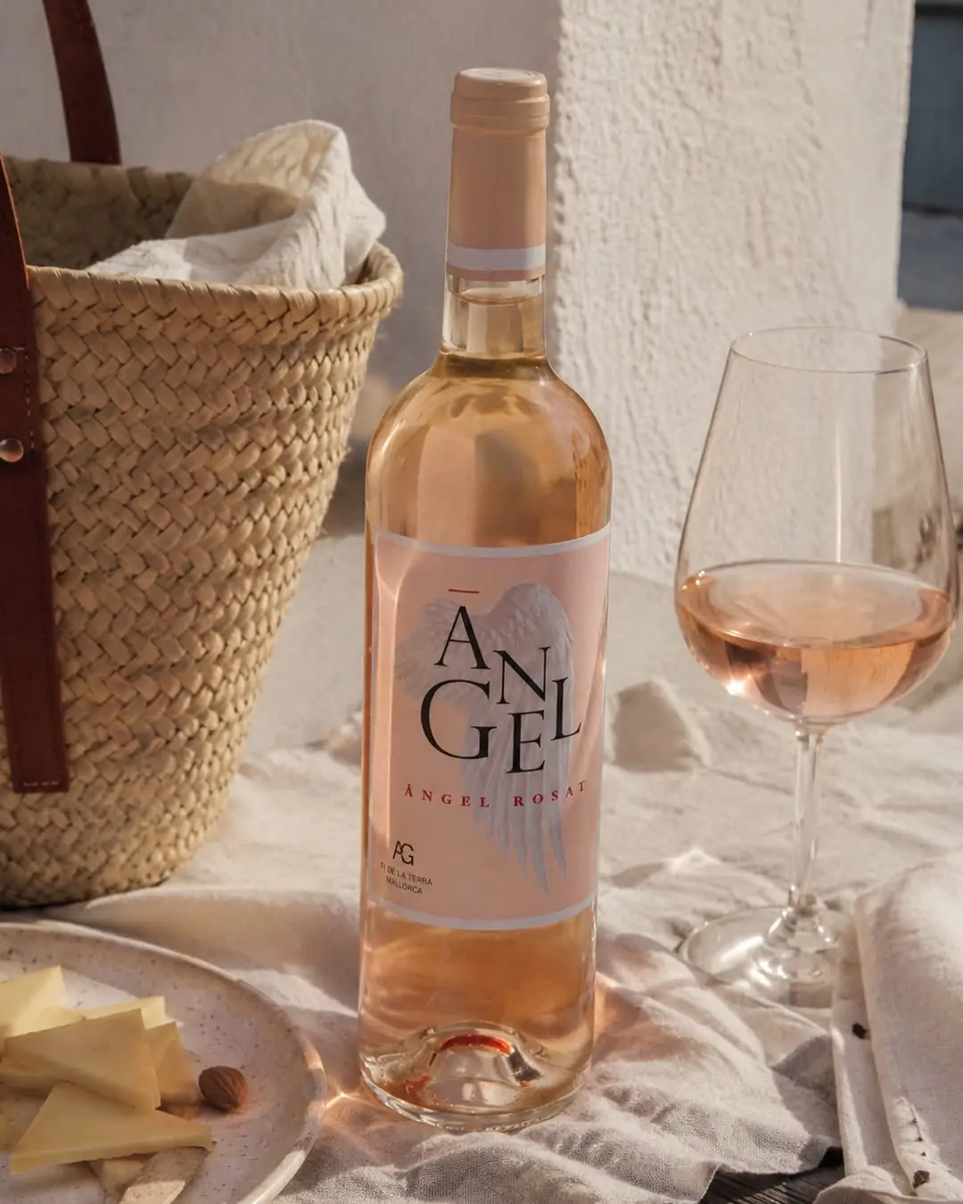 A bottle and glass of Bodegas Ángel rosé beside a straw bag