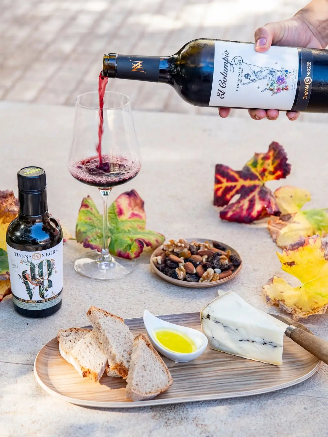 Pouring Tianna Negre red wine over bread, cheese and olive oil