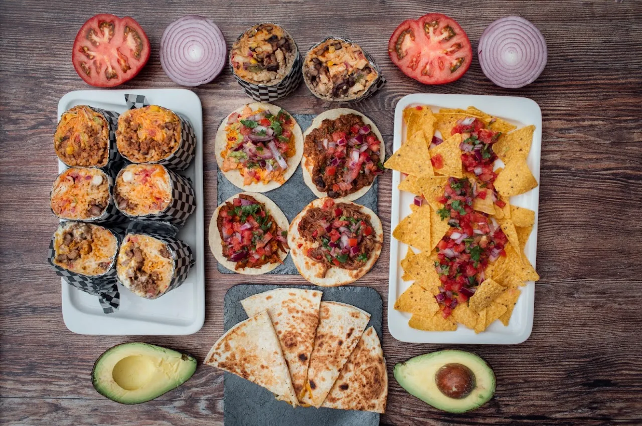 An overhead spread of stuffed peppers, quesadillas, and nachos with tomato and onion