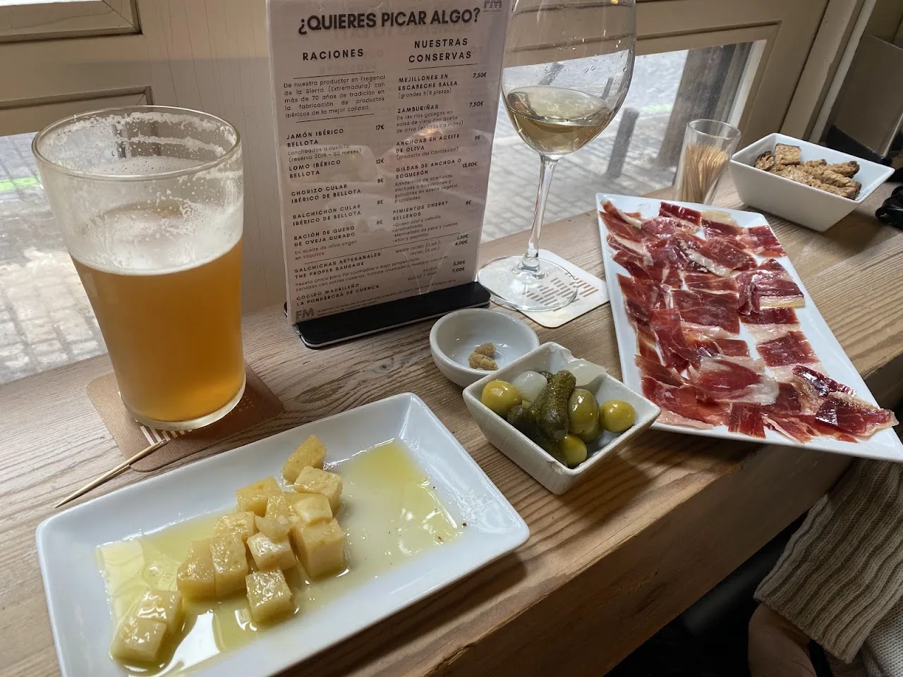 A glass of beer with olives, bread cubes, and a plate of ham