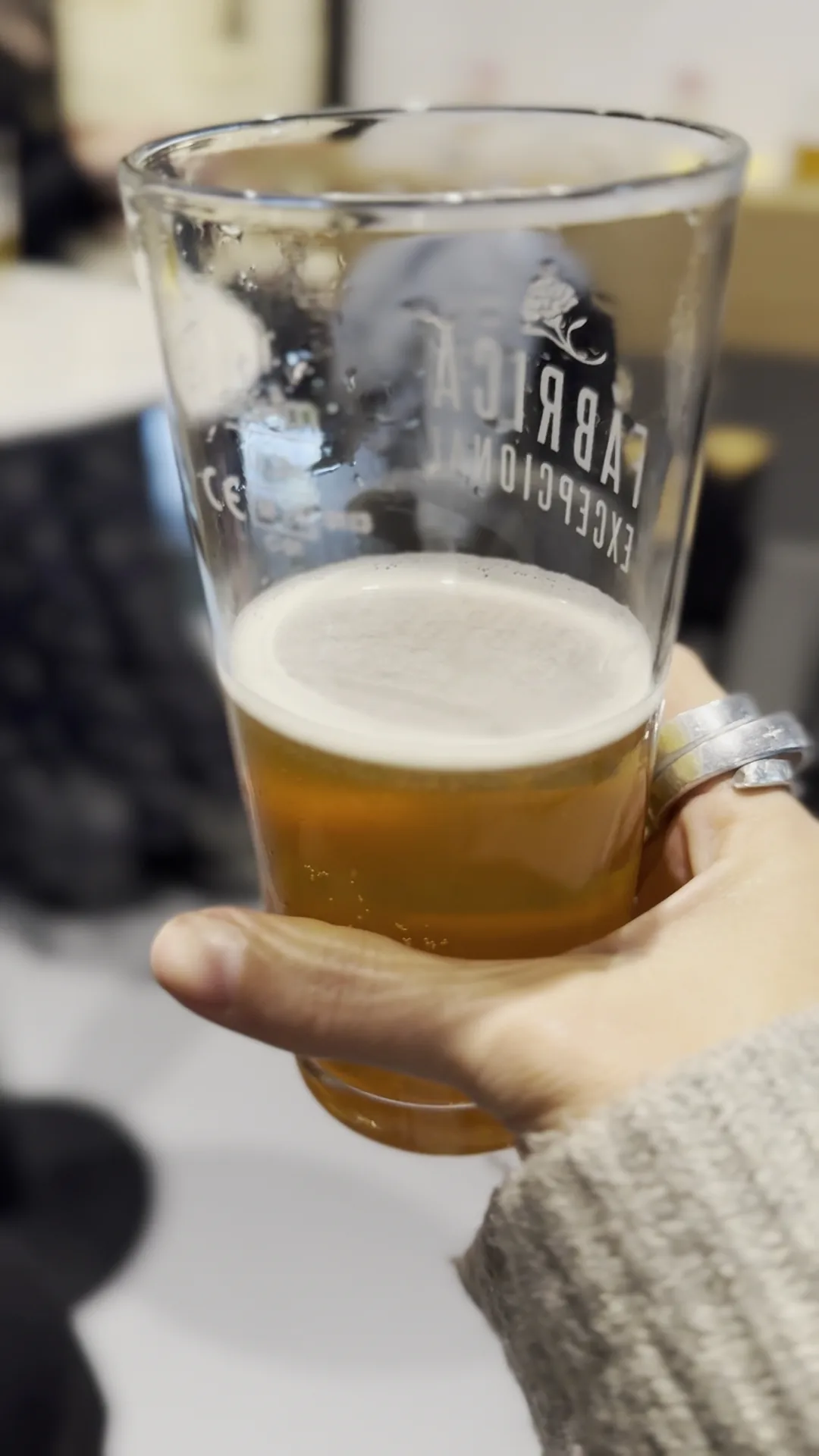 A hand holding a glass of beer with a thick foam head