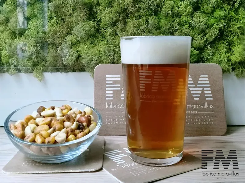 A glass of beer with a bowl of peanuts
