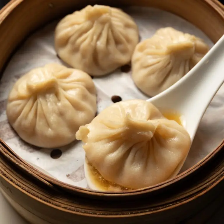 Close-up of steamed xiaolongbao dumplings in a bamboo steamer, one lifted on a white spoon with broth pooling inside, at Fan Dim Sum