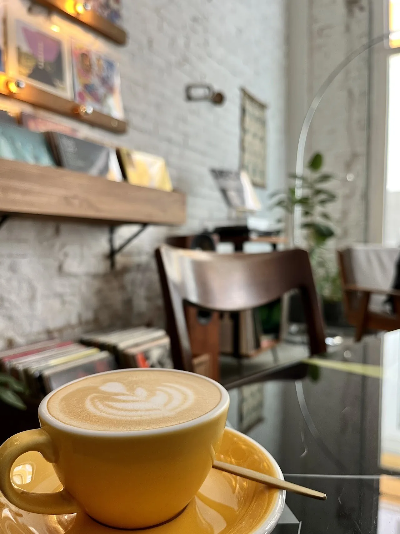 A latte with art in a yellow cup on a table with shelves of records behind