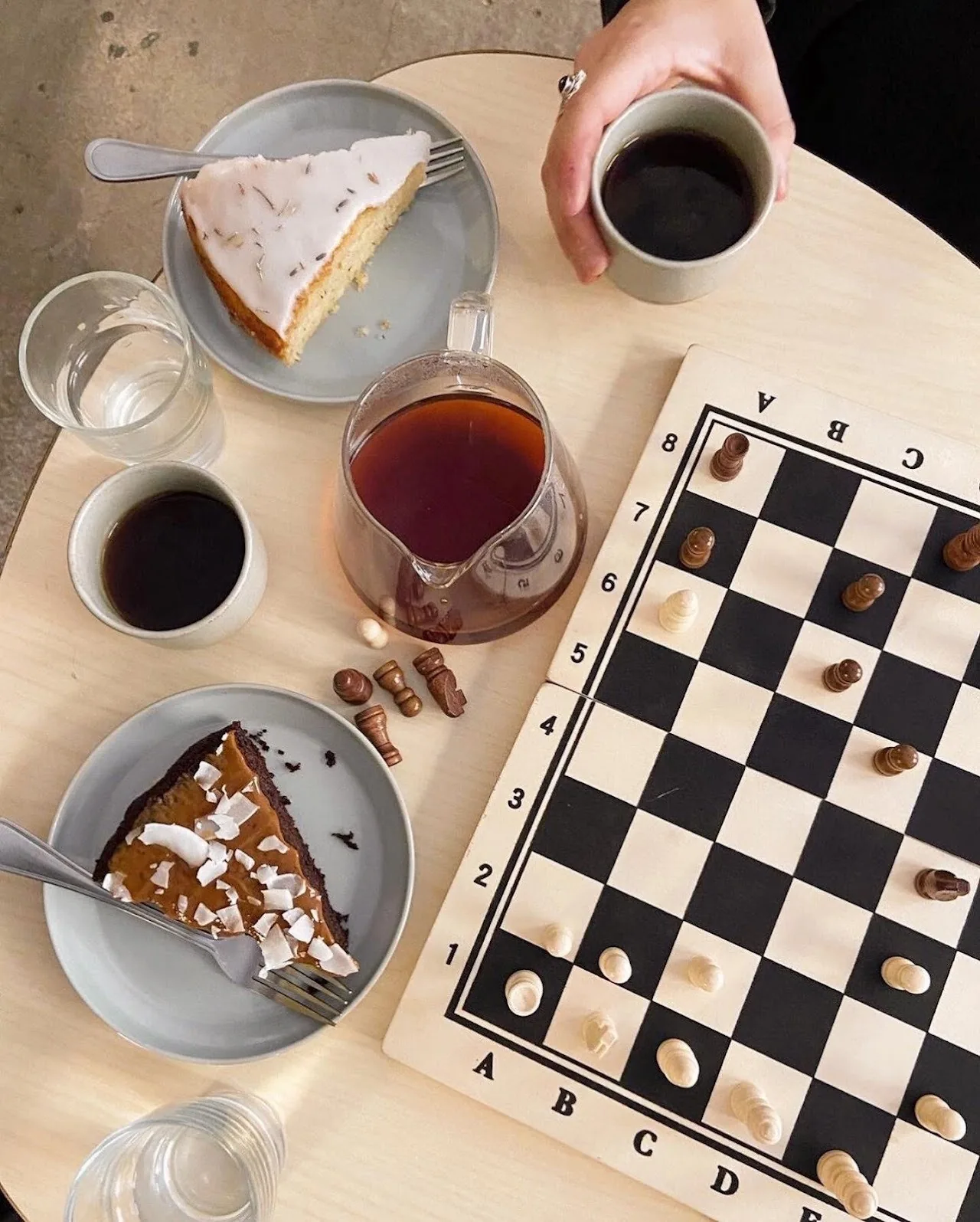 Cups of coffee, slices of cake and a chess board on a round table seen from above