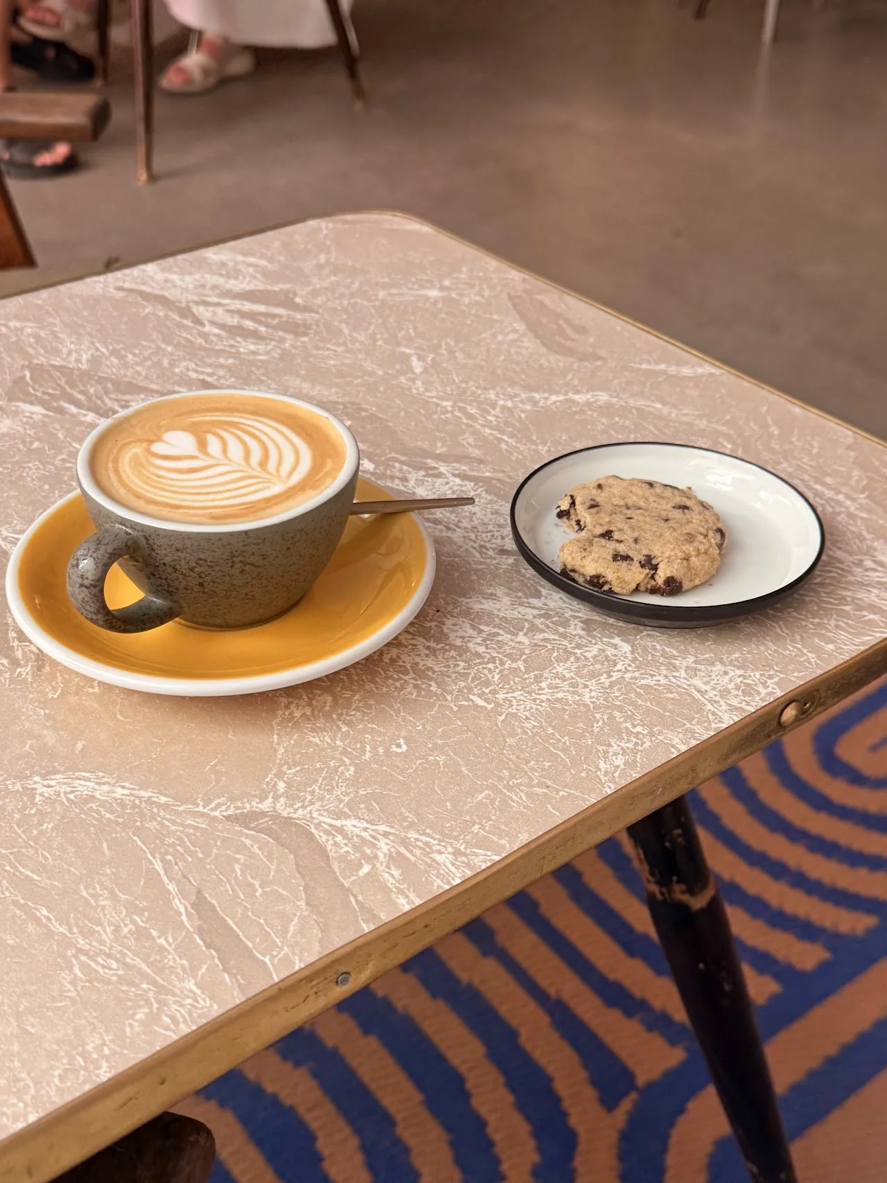 A latte with foam art next to a cookie on a marble table