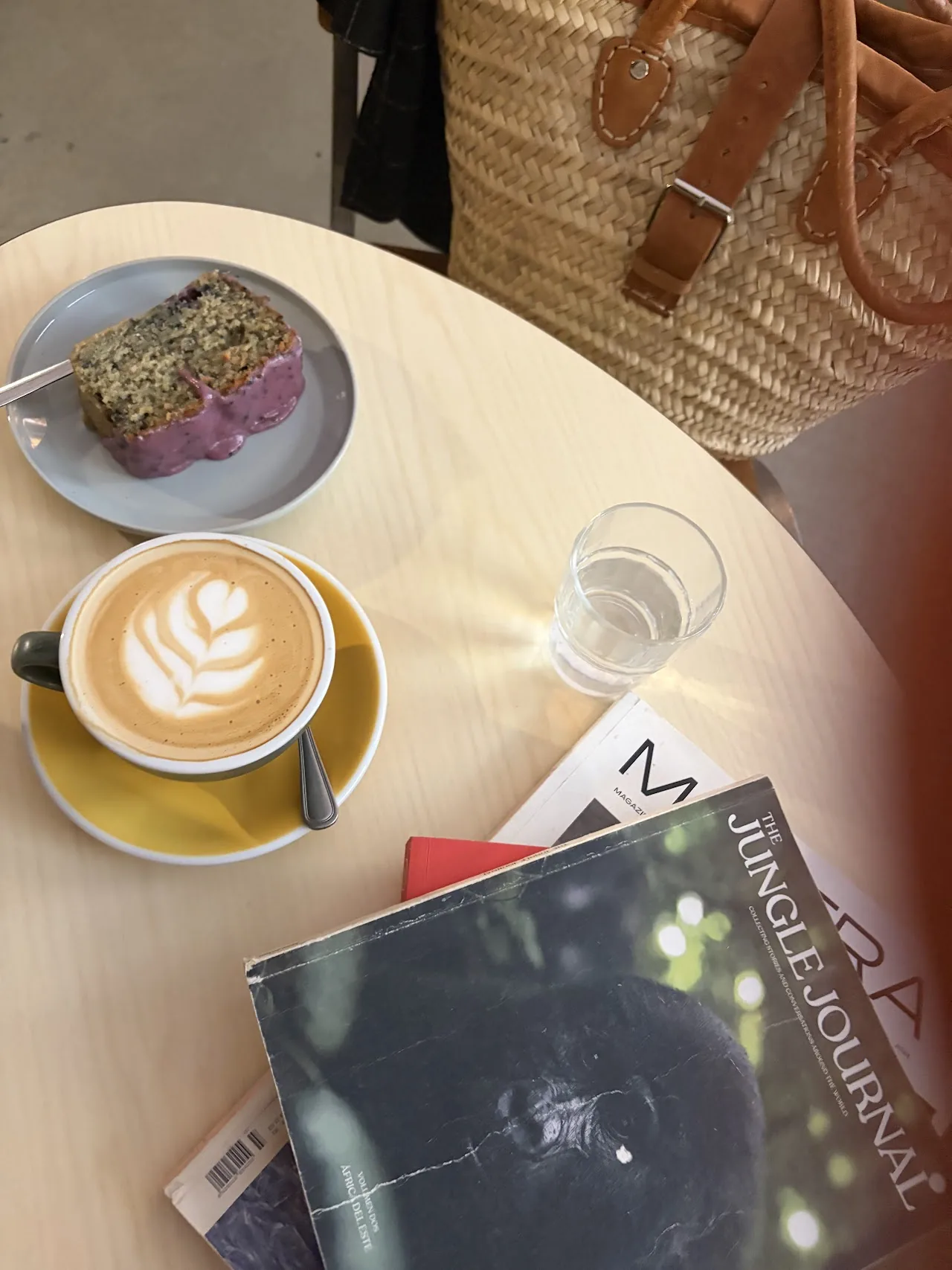 A slice of cake on a plate next to a latte with foam art