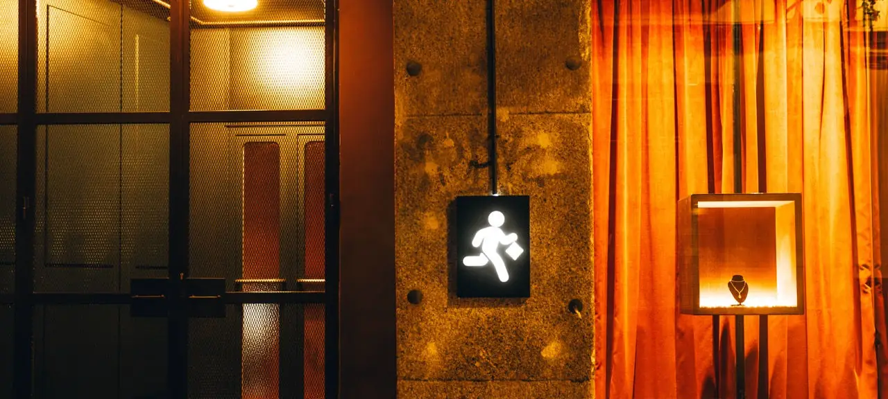 Dimly lit bar entrance at night: mesh-glass doors, a stone pillar with an illuminated running-man sign, warm orange curtains and a lit display niche holding a necklace