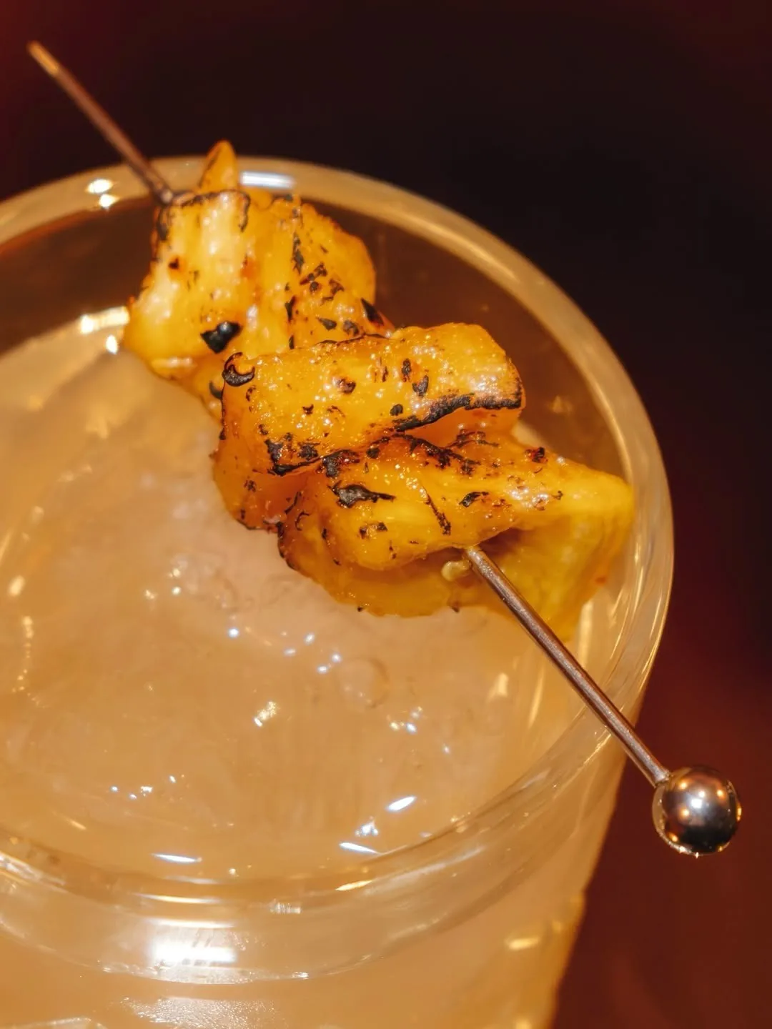 A close view of a cocktail with a grilled skewer garnish and ice
