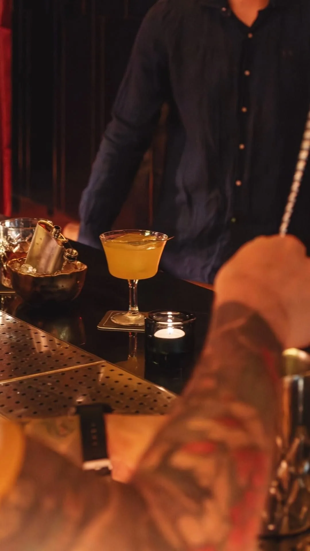 A bartender pouring an orange cocktail into a glass at a bar