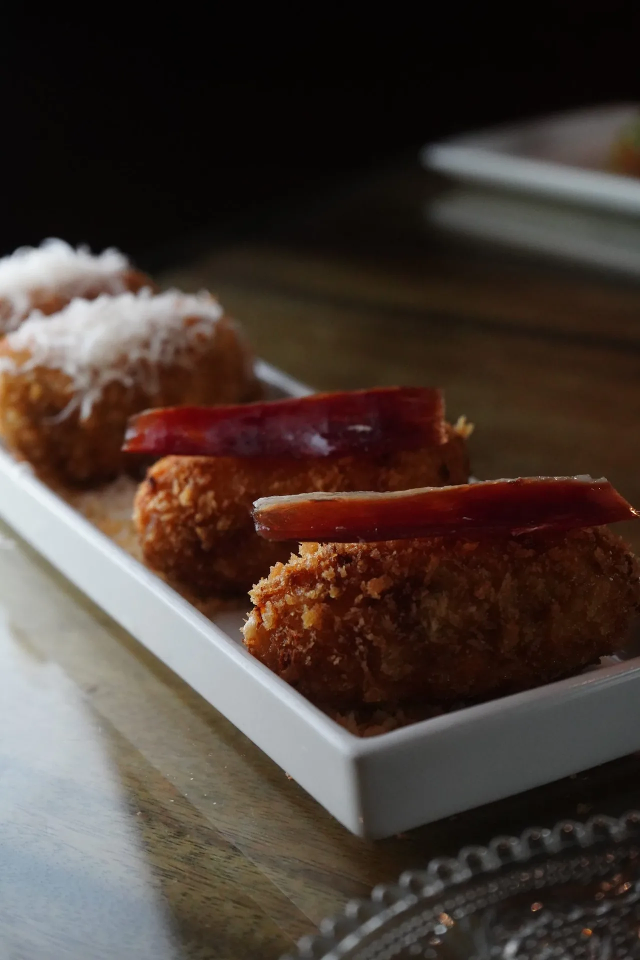 Golden breaded croquetas with a strip of cured ham on a white rectangular dish
