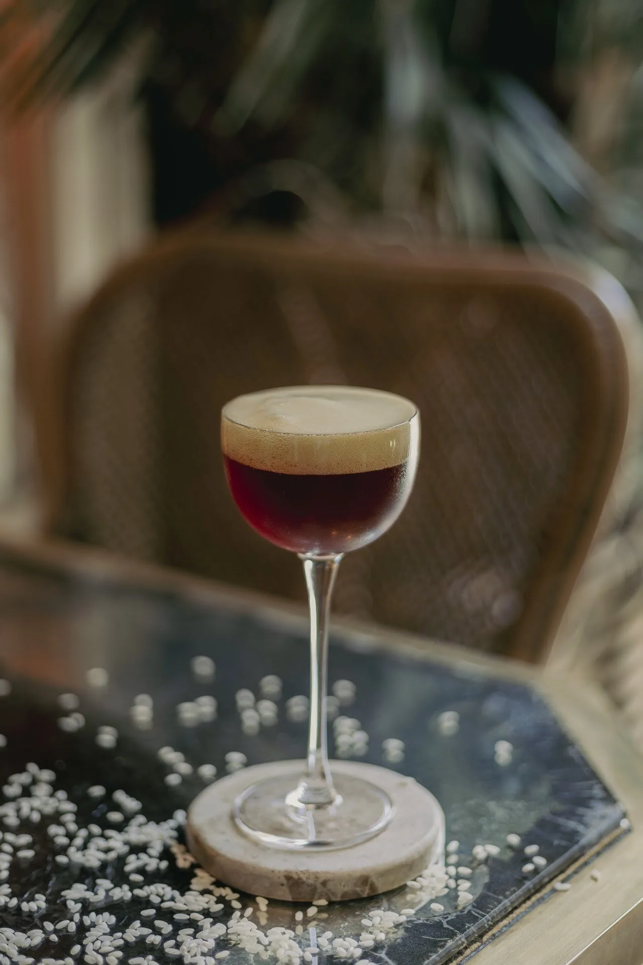 A dark espresso martini in a coupe glass on a table with a chair behind it