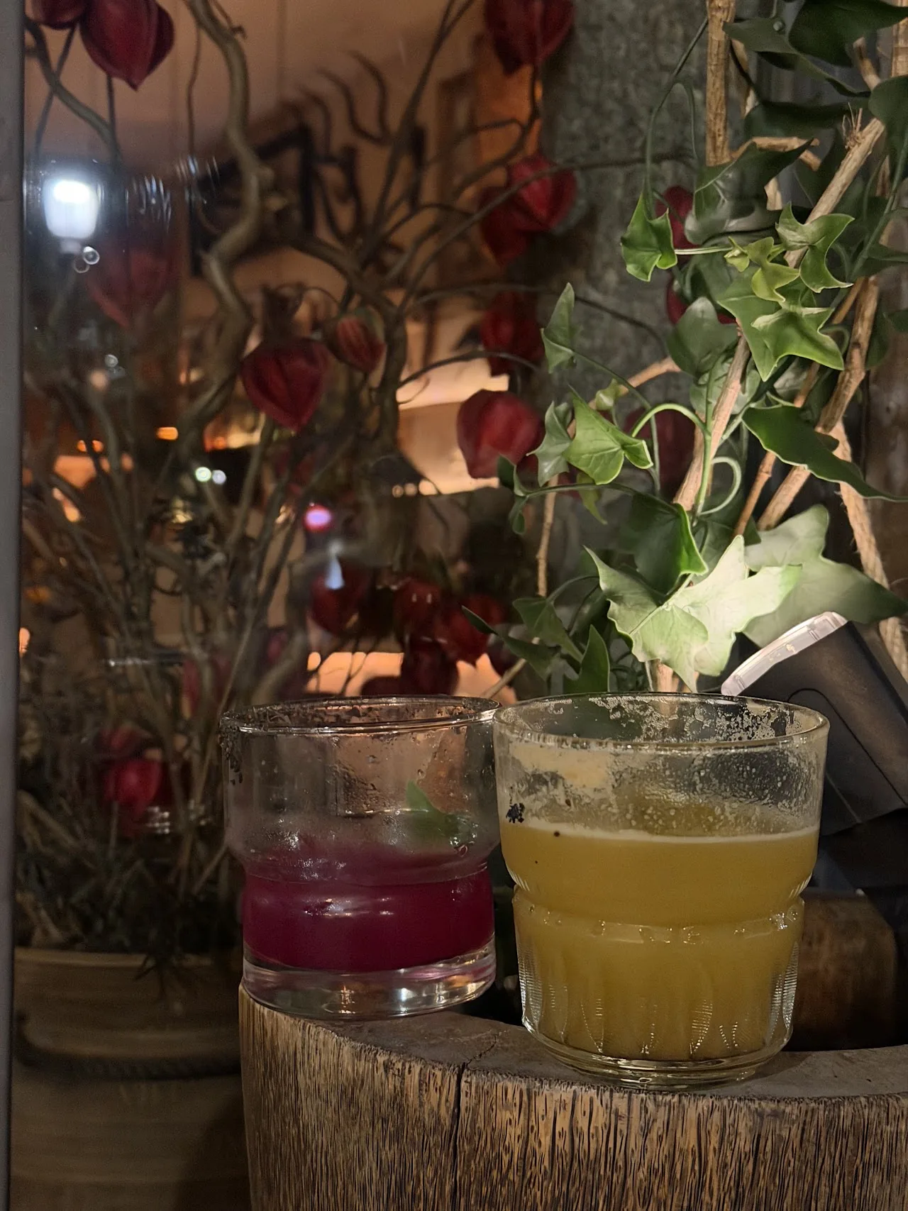 Two cocktails, one pink and one green, served on a tree-stump table