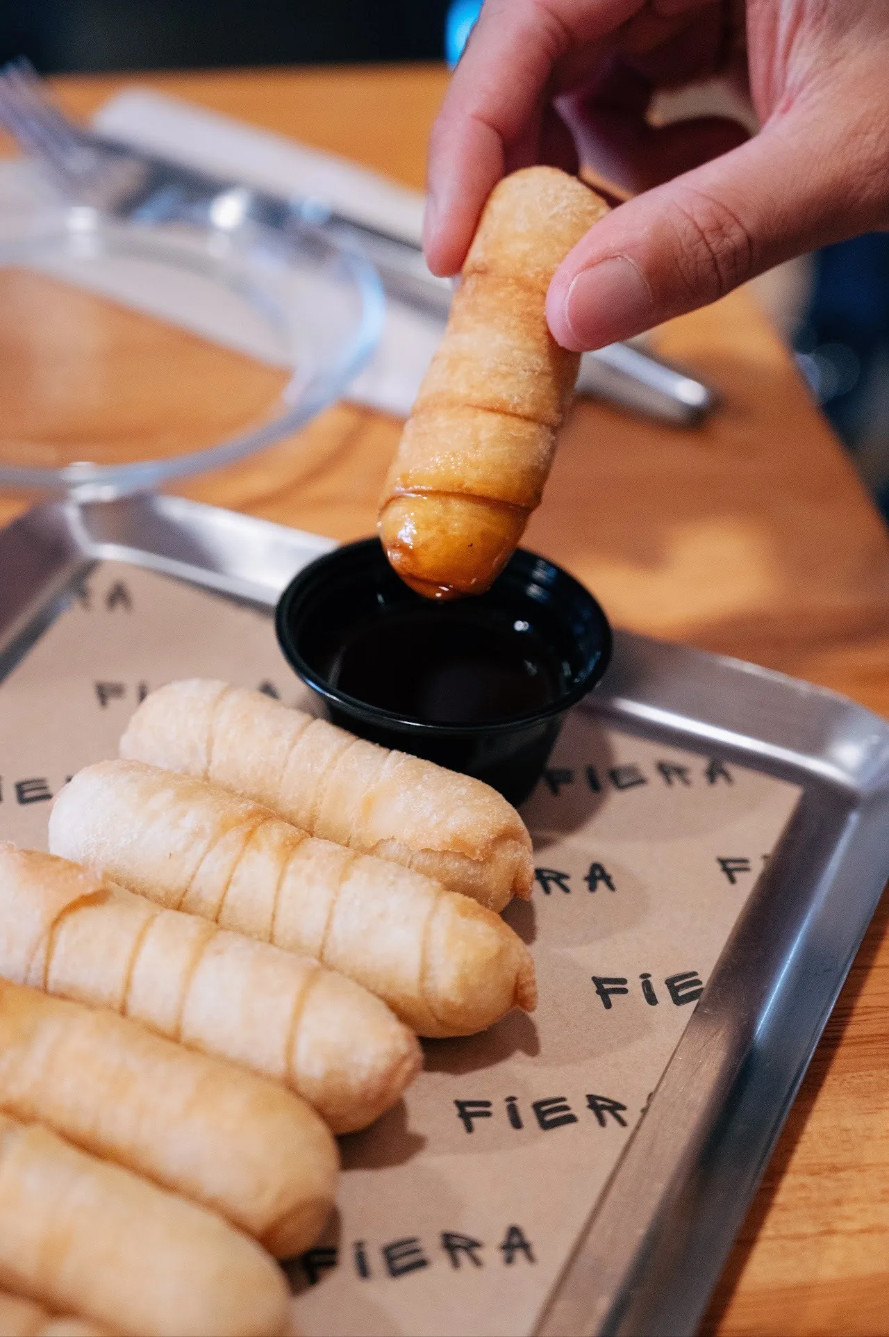 A golden tequeño being dipped in a dark sauce beside other tequeños