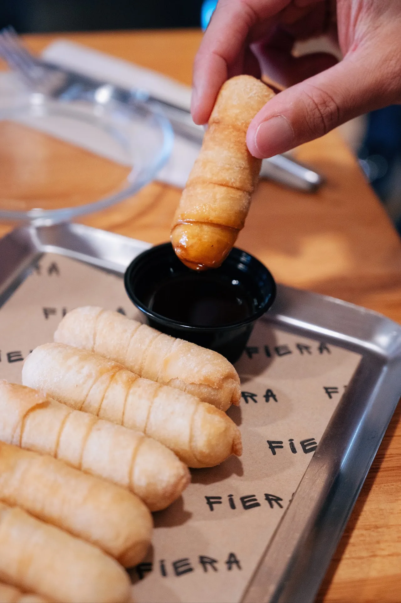 A hand dipping a golden fried corn rib into dark sauce