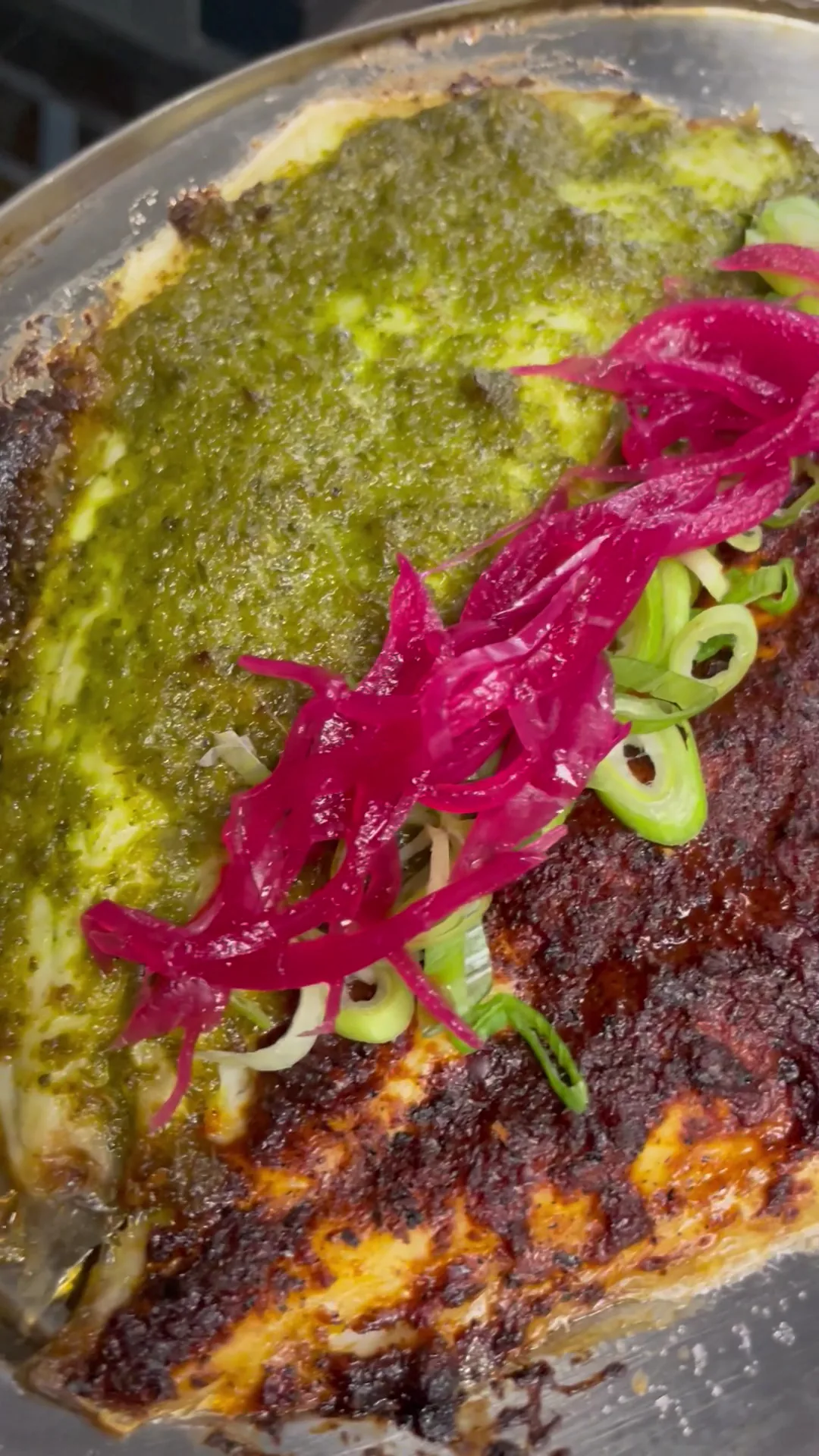 A tostada topped with green sauce and pickled red onions