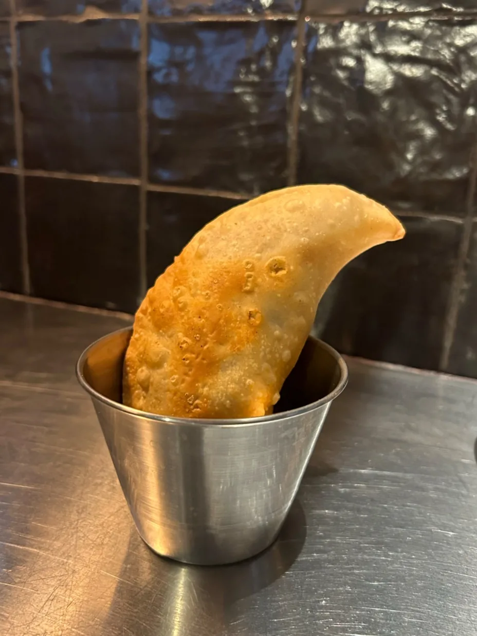 A golden empanada standing in a small metal cup