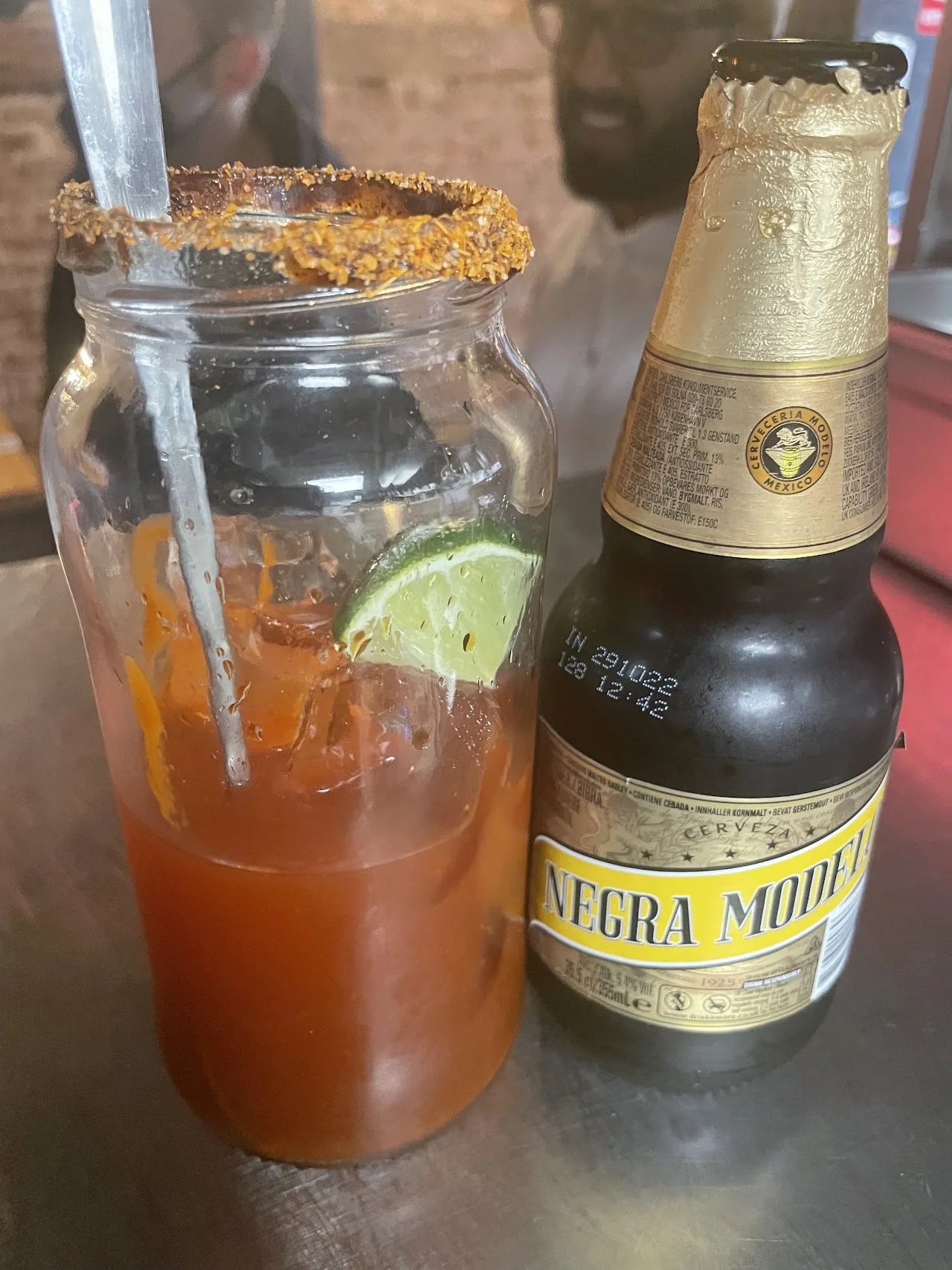 A michelada cocktail in a chili-rimmed glass next to a beer bottle