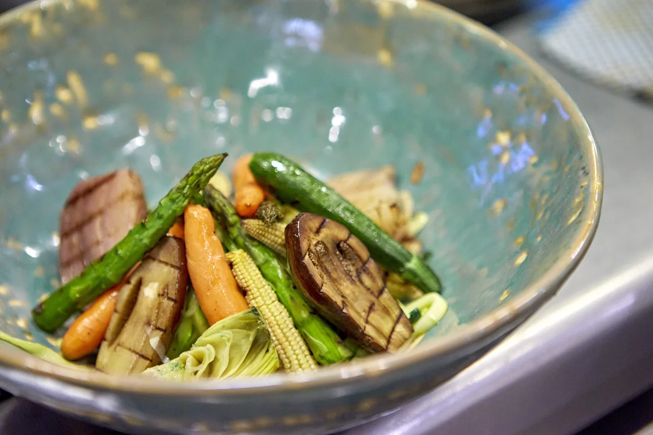 A blue-green bowl of grilled vegetables including carrots and aubergine