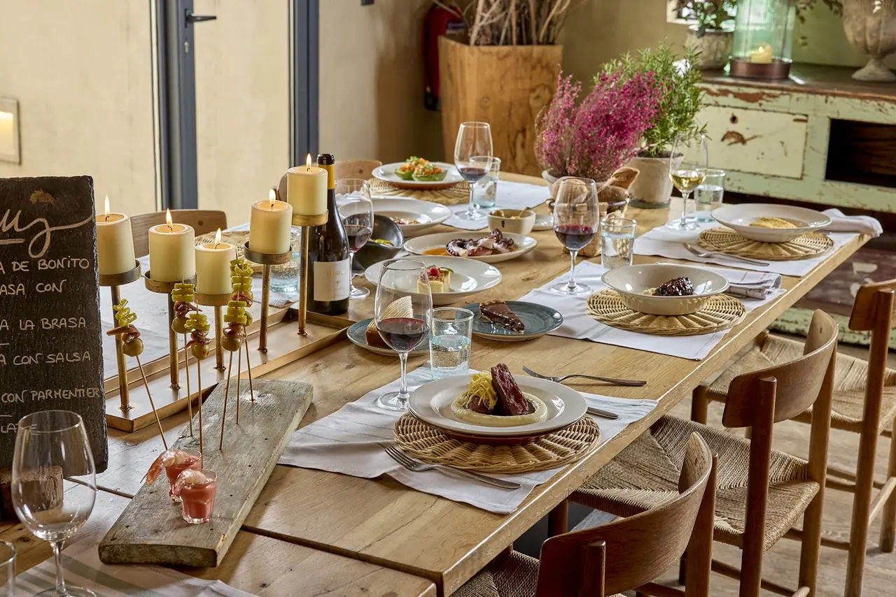 Long wooden table set with multiple plated dishes, candles and wine glasses