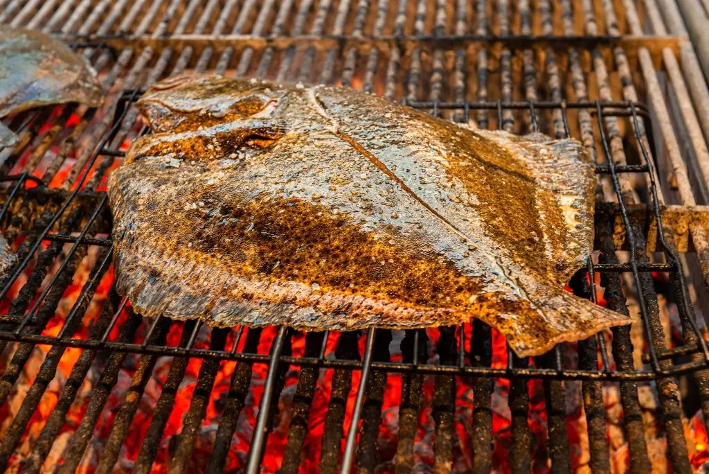 Whole flat fish cooking on a wood-fired grill over glowing coals