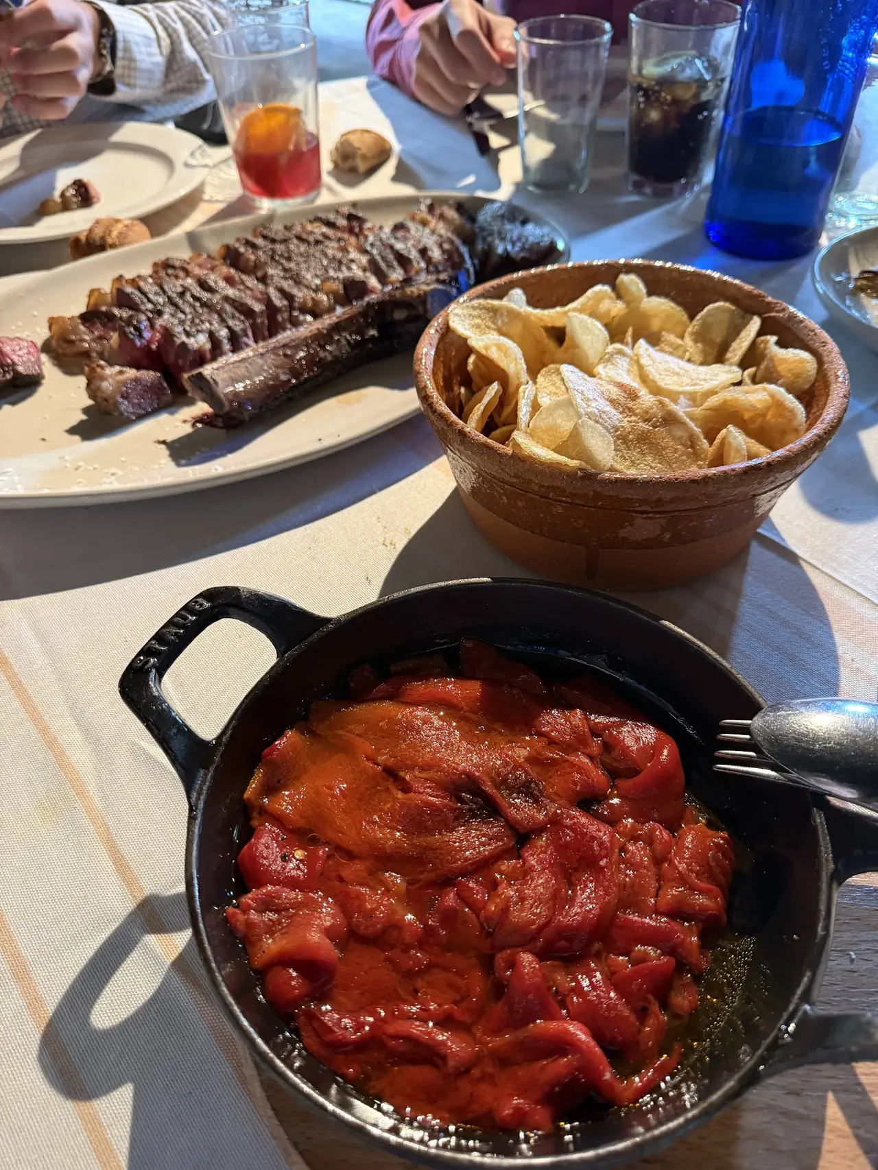 Roasted red peppers in a cast iron pan, with potato chips and sliced steak on the table