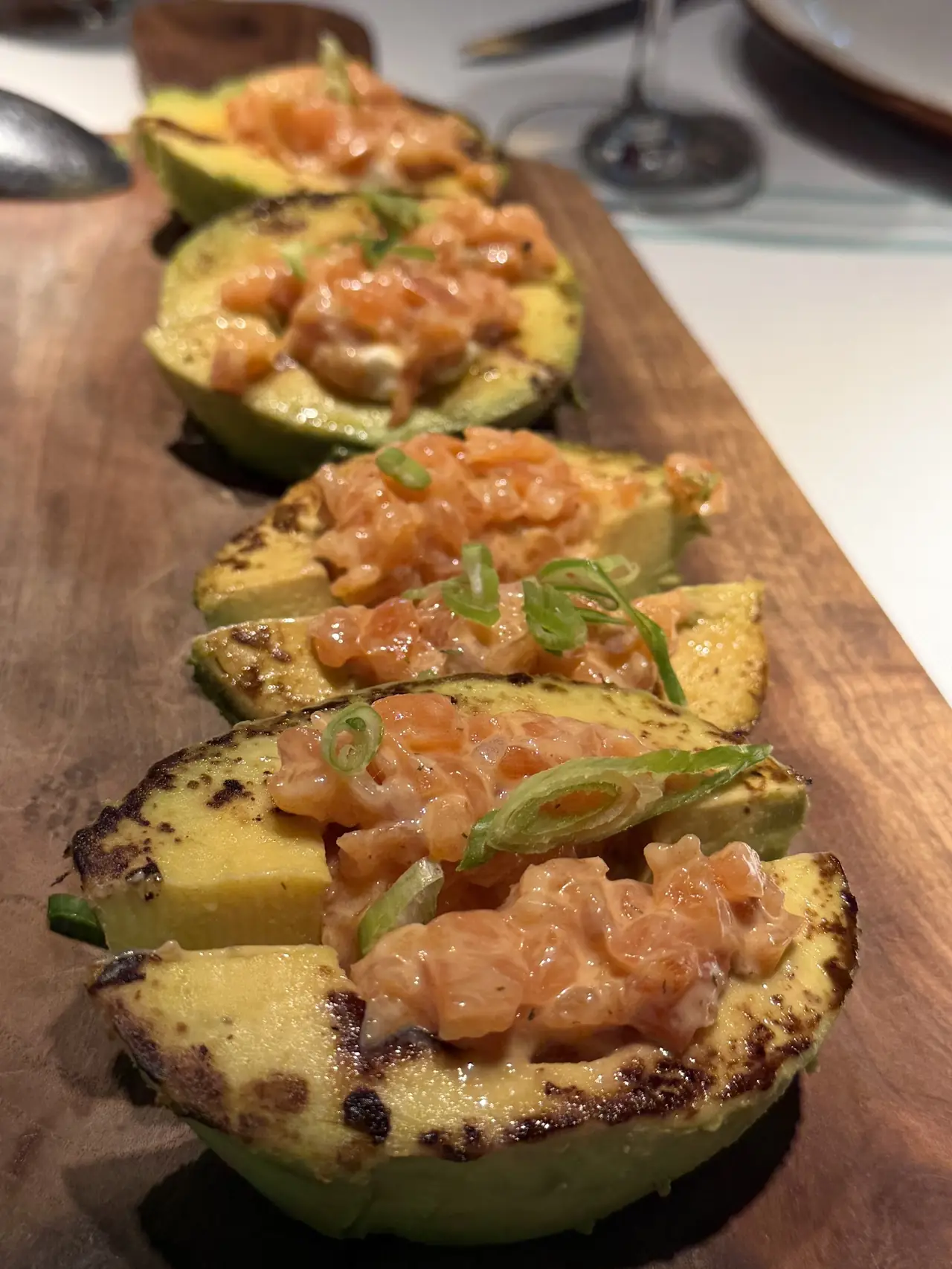 Grilled avocado halves topped with salmon tartare and scallion on a wooden board