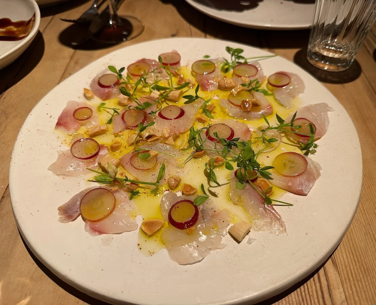 A large white plate of sliced fish with fruit and herbs