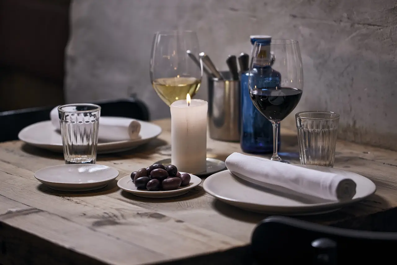 Small plate of black olives beside a candle, with poured glasses of white and red wine on a wood table