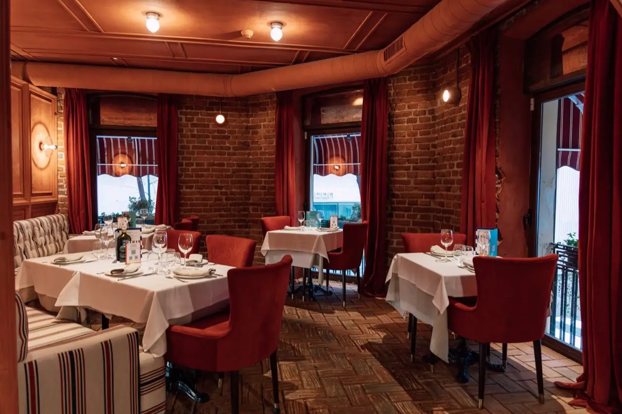 Intimate dining room with white-clothed tables, red velvet armchairs, exposed brick walls, red curtains and parquet flooring