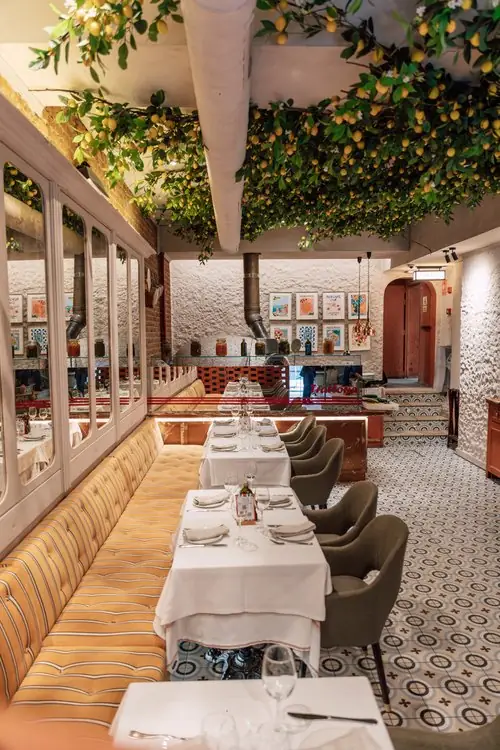 Narrow dining room with faux lemon-tree canopy overhead, yellow striped banquette and white-clothed tables on patterned tile floor