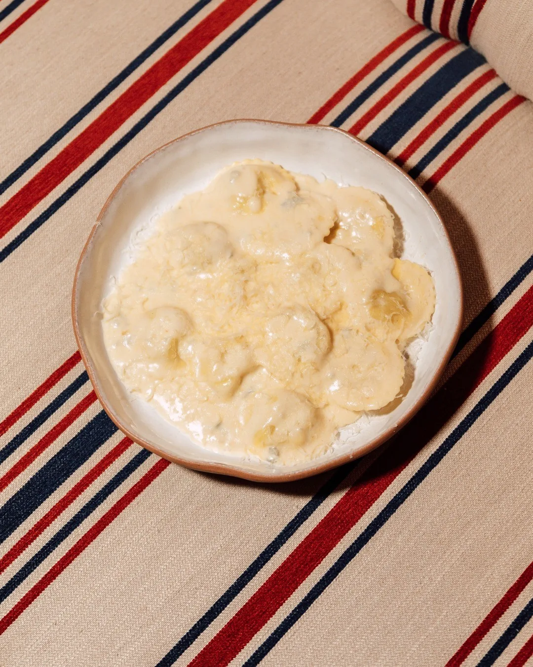 A shallow bowl of pasta in a creamy white sauce on a striped cloth