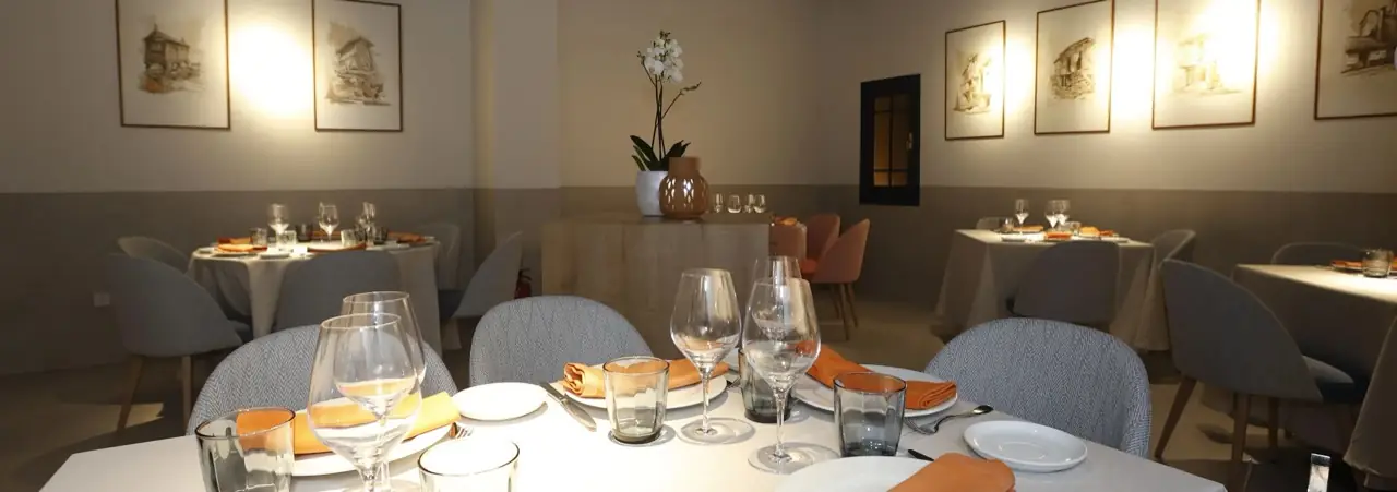 Dining room with round and square tables laid with white cloths, orange napkins, wine glasses and framed watercolour prints on the walls