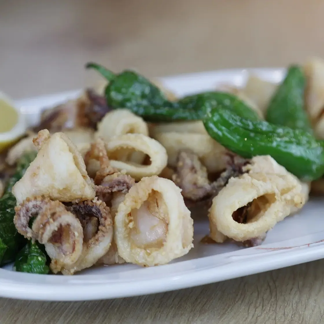 A white plate of fried squid rings with green peppers and a lemon wedge