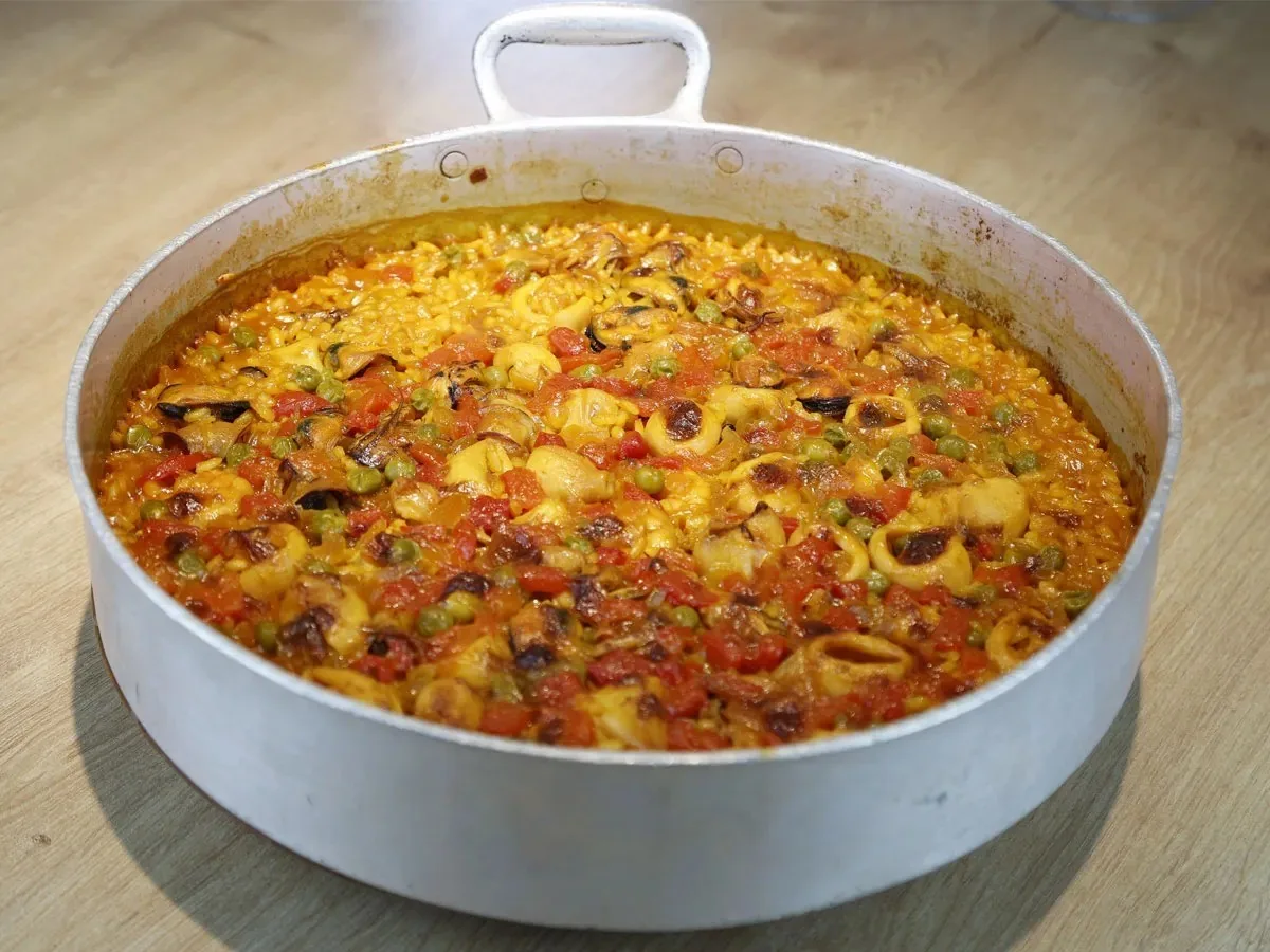 A wide aluminium pan of golden rice with peas and squid on a wooden table