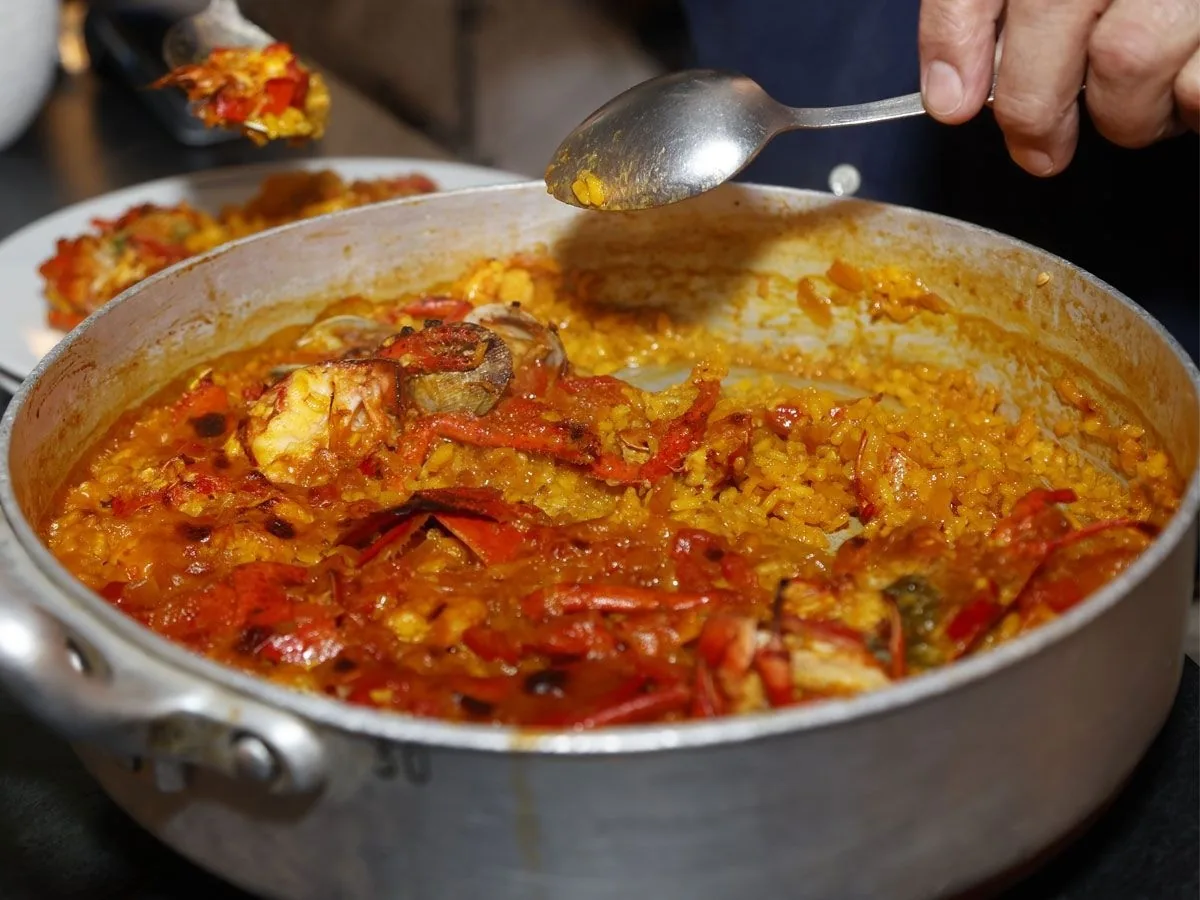 A spoon serving red-orange rice from a large pan
