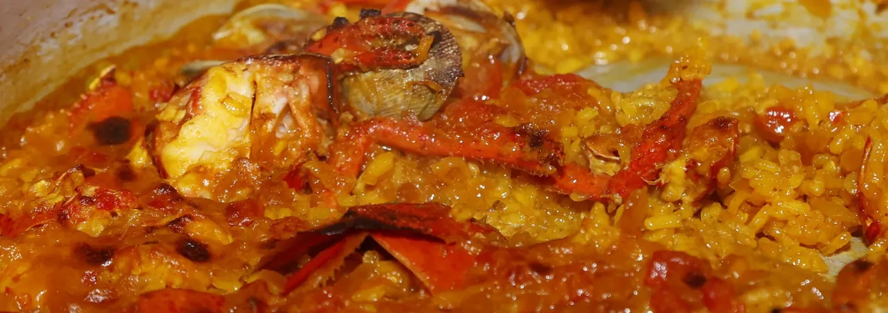 Close view of orange rice with shellfish and a clam in a pan