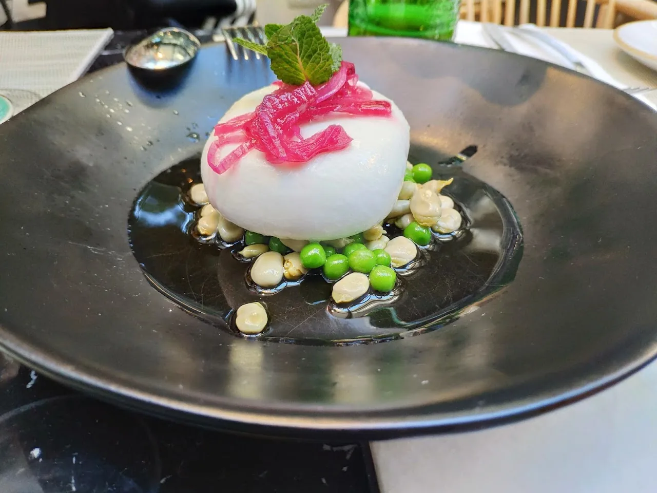 A round dish with a pink beetroot swirl, white cream, and green peas