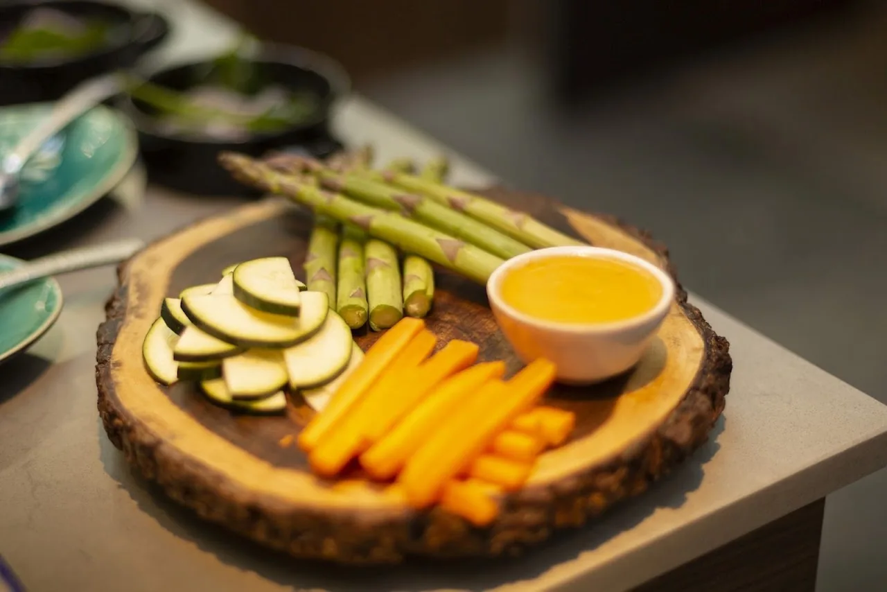 A wooden board with asparagus, zucchini, carrot sticks, and a dip