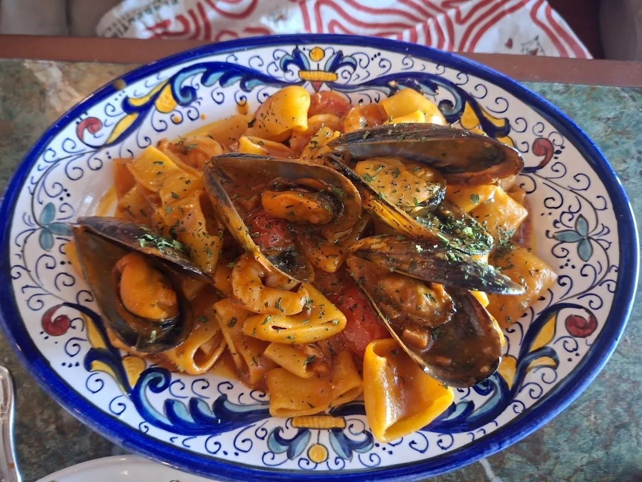 A blue and yellow patterned plate of pasta with mussels and orange sauce