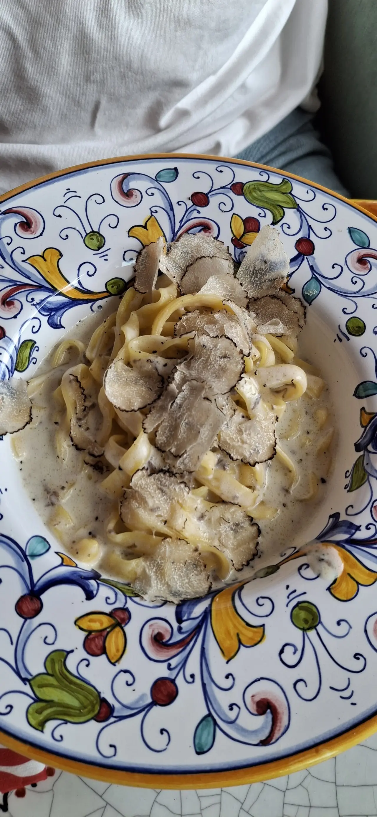 A creamy pasta dish topped with shaved truffle, served on a Sicilian-patterned plate.