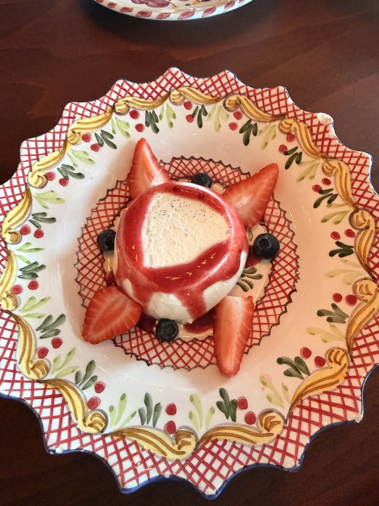 A panna cotta-style dessert with fresh strawberries and berries on a decorative plate.