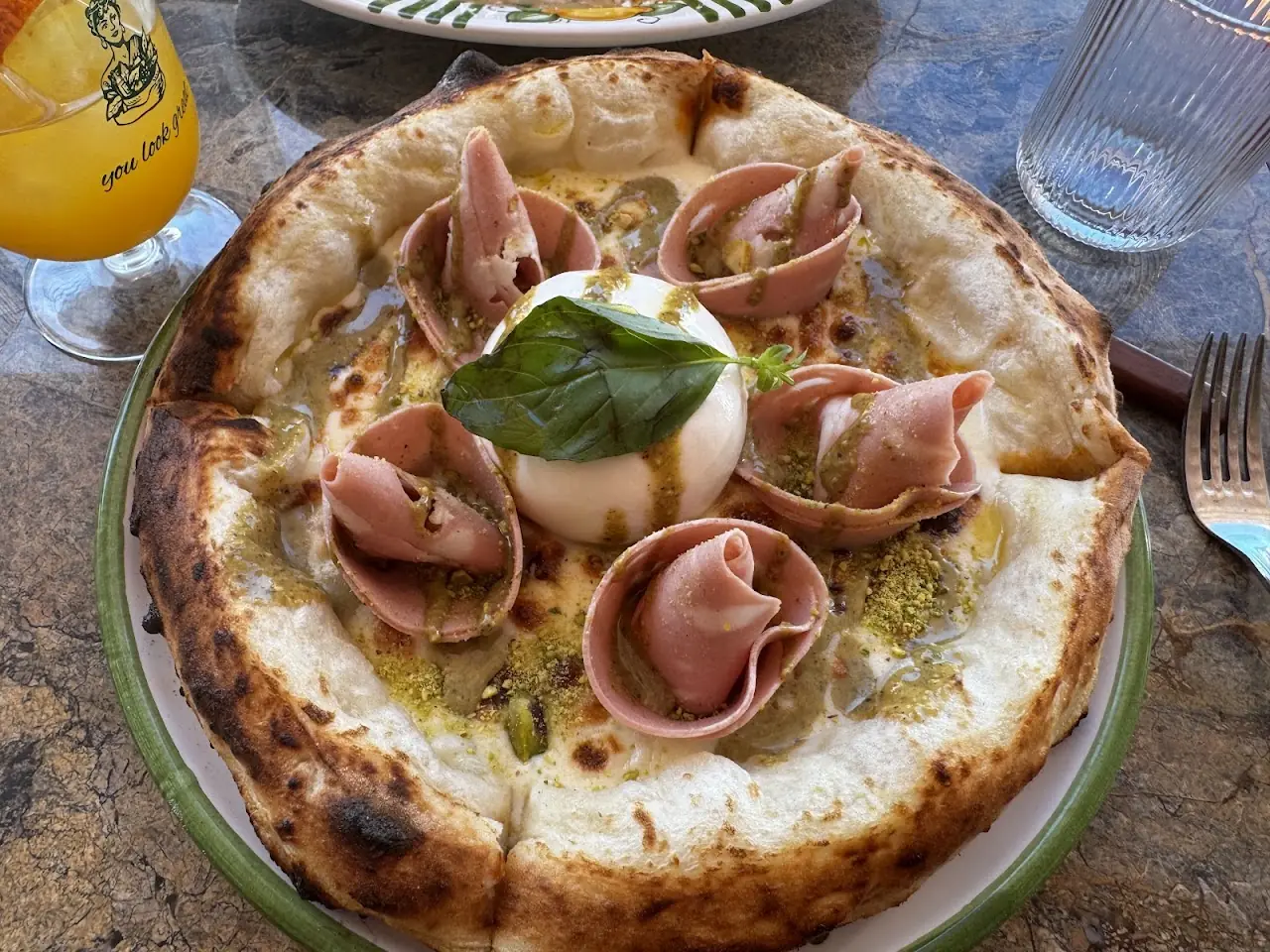A pizza topped with a whole burrata and rolled prosciutto, garnished with basil.