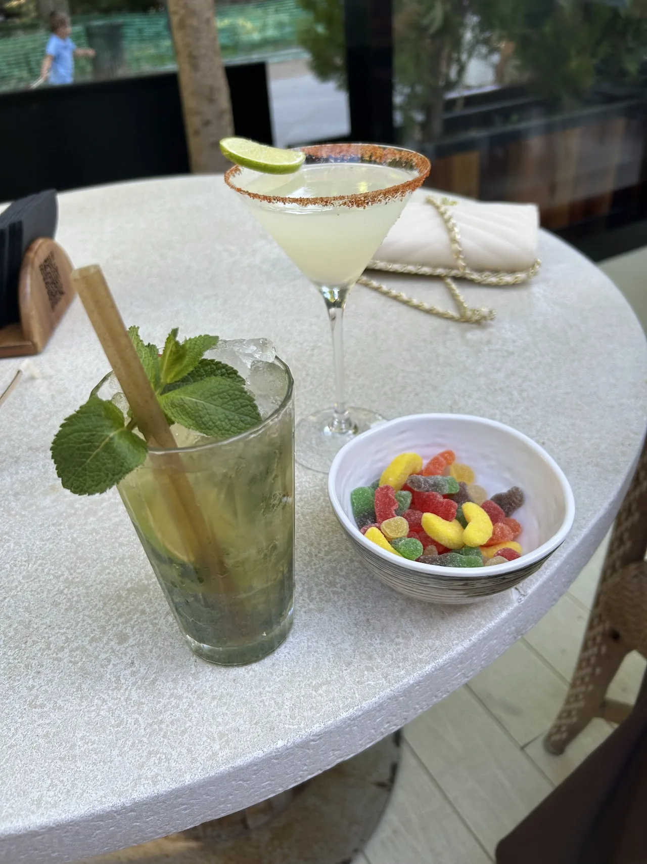 A mojito and a margarita glass with a bowl of mixed fruit