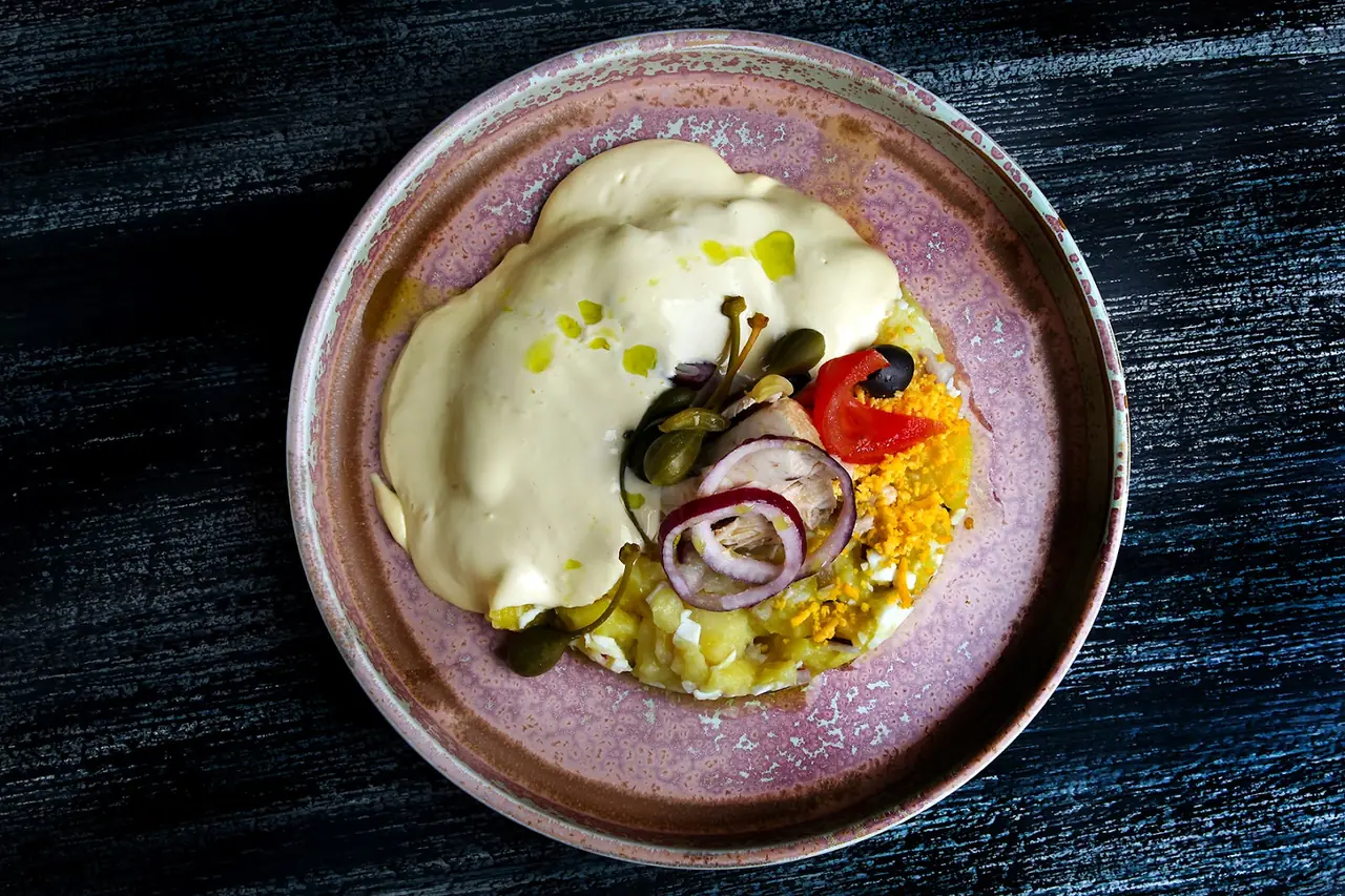 Potato salad topped with mayonnaise, capers, red onion, olive, pepper and grated egg on a rustic plate