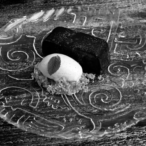 A chocolate bar dessert beside a scoop of cream with a mint leaf, on a decorative etched plate